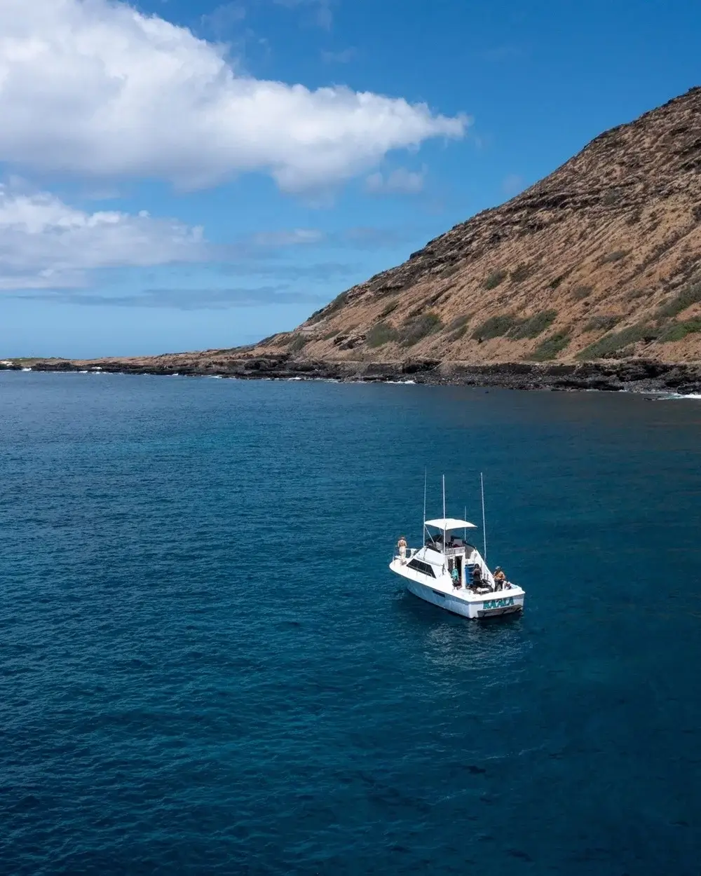 A white boat on deep blue ocean near a rocky coastline under a bright sky.
